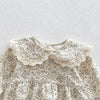 A white floral lace cotton romper for a baby girl with ruffled details.