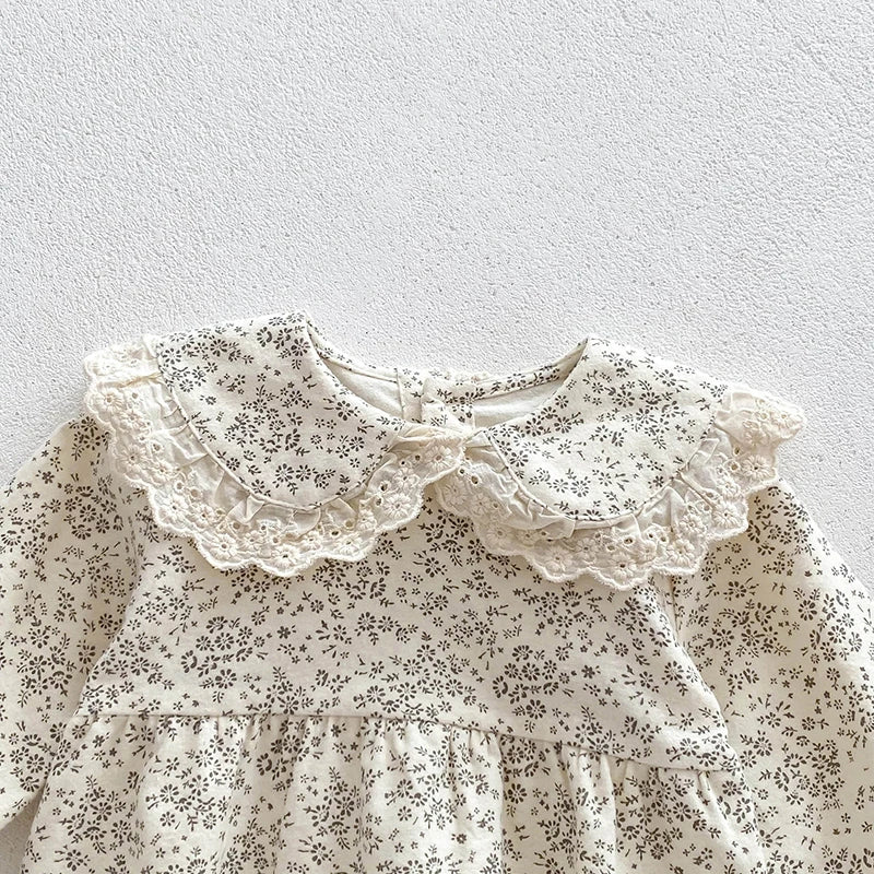 A white floral lace cotton romper for a baby girl with ruffled details.
