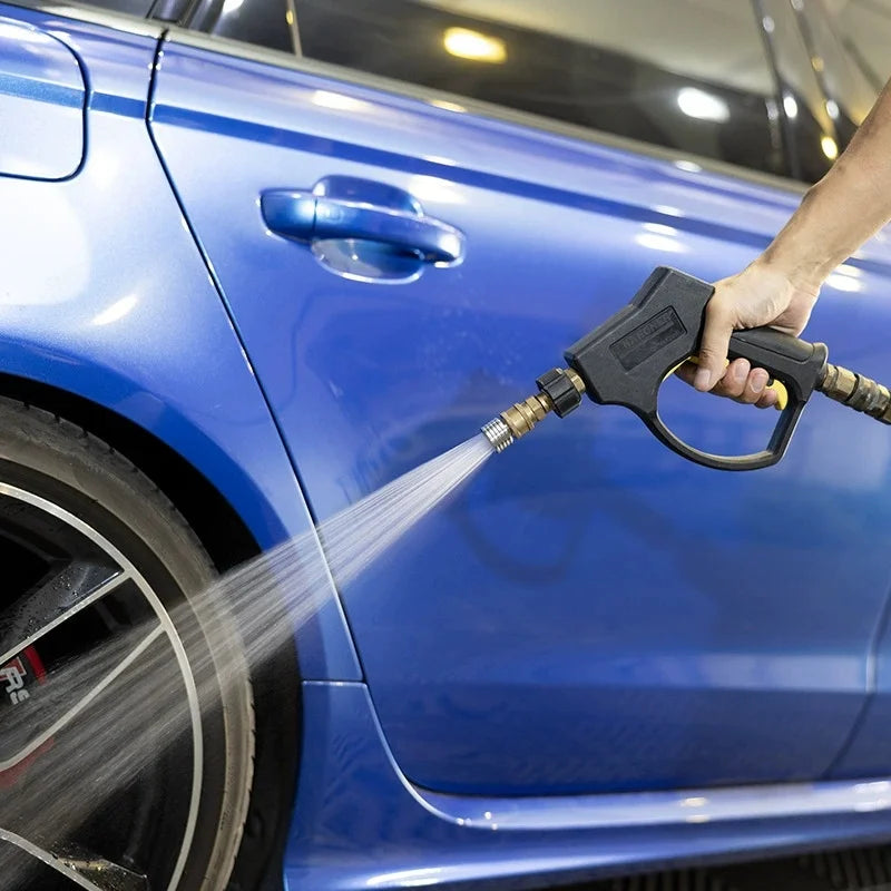 A hand sprays water onto a blue car's body with a stainless steel high-pressure washer nozzle.