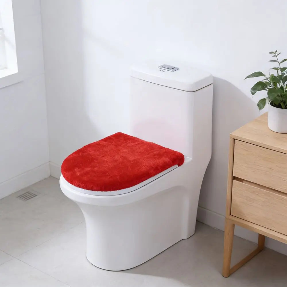 A white toilet with a bright red flannel seat cover resting on it, next to a wooden cabinet.