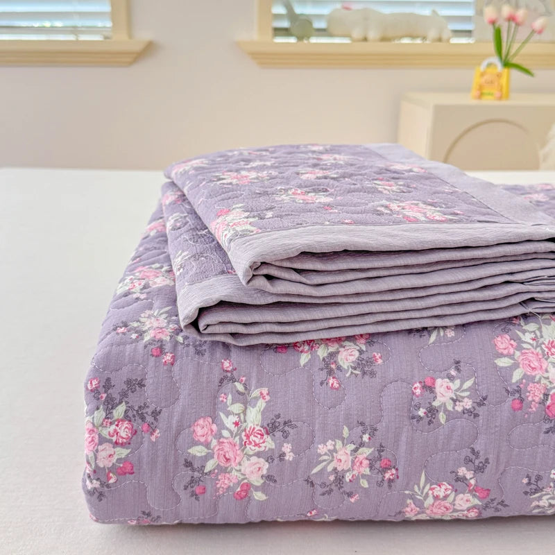 A stack of purple floral quilted bedspreads or coverlets on a white surface.