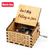 A vintage hand-crank wooden music box with a lid engraved 'Can't Help Falling in Love' and decorative wood grain.