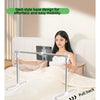 A woman is using an adjustable foldable tablet stand designed for easy movement on a bed.