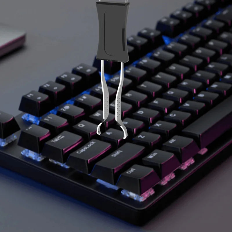 A close-up view of a black mechanical keyboard with a metal keycap puller and adjuster tool inserted into a keycap.