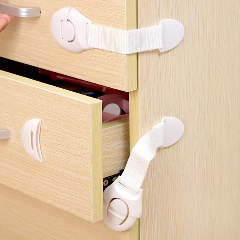 White child safety cabinet locks installed on a light wood drawer and door.