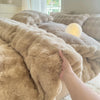 A hand is touching a fluffy beige fleece duvet cover with a rabbit design, resting on a bed.
