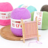 A collection of pink, purple, and green fine yarn balls next to a wooden knitting needle tool.