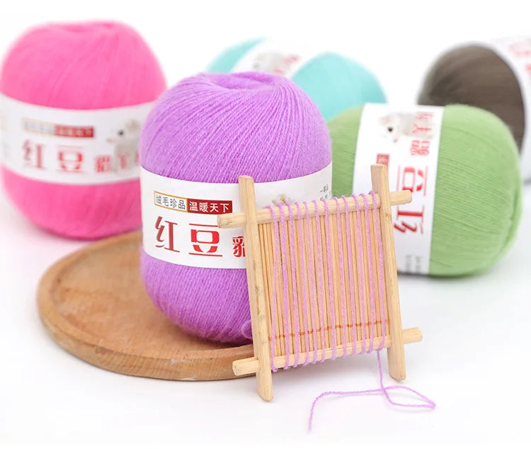 A collection of pink, purple, and green fine yarn balls next to a wooden knitting needle tool.
