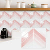 Pink and white herringbone marble peel-and-stick wall tiles displayed on a wooden shelf.