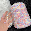 A hand is holding a skein of hand-dyed variegated cotton blend yarn featuring pink, yellow, and purple colors.