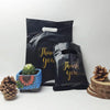 A set of black thank you gift bags with gold lettering and natural elements like pinecones and succulents.