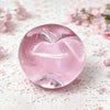 A translucent pink fruit-shaped squeeze toy for stress relief resting on white lace fabric.