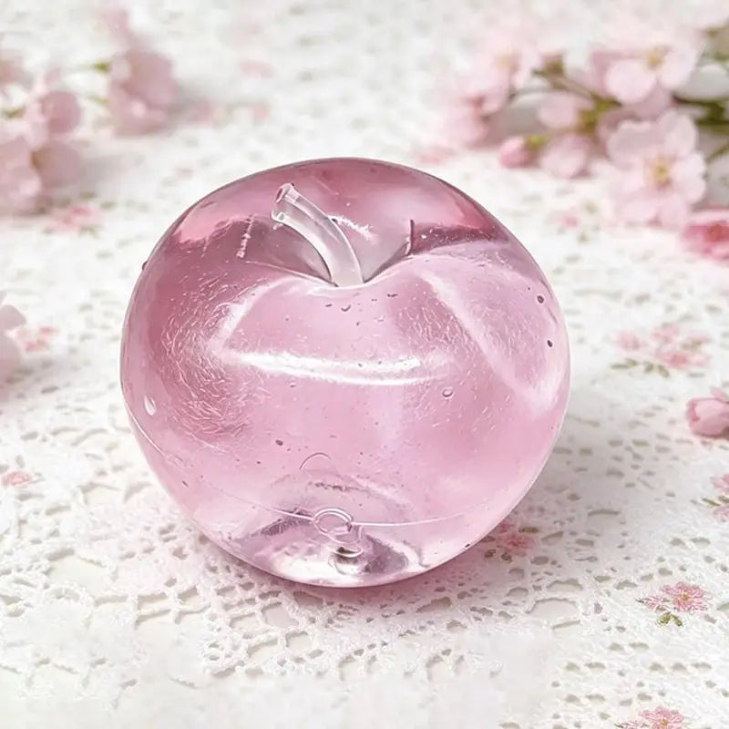 A translucent pink fruit-shaped squeeze toy for stress relief resting on white lace fabric.
