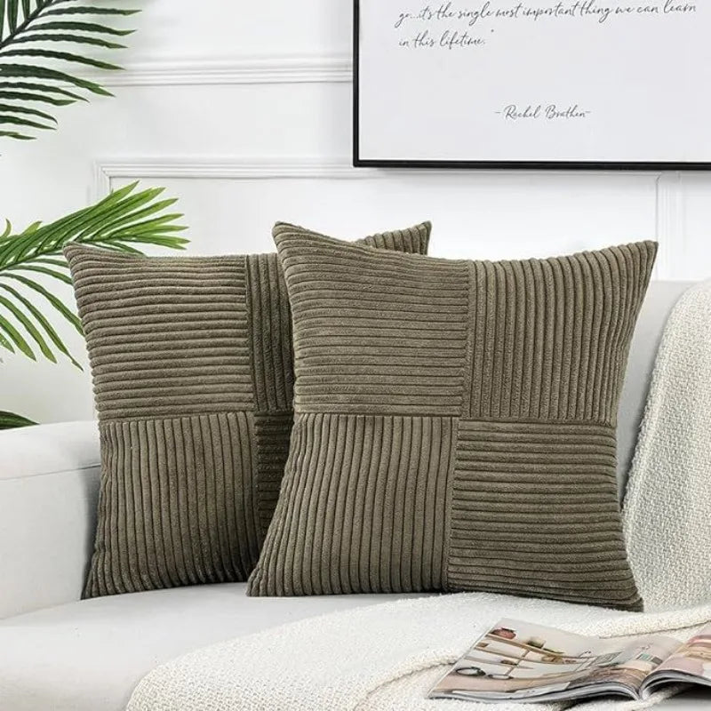 A set of two olive green corduroy patchwork throw pillow covers with vertical ribbed texture on a white sofa.