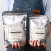 A person holds two bags of natural soy wax flakes for DIY candle making, labeled with melting points and features.