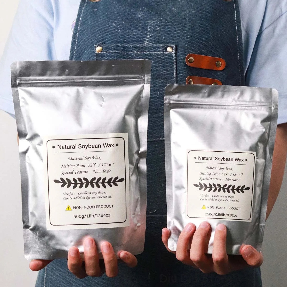 A person holds two bags of natural soy wax flakes for DIY candle making, labeled with melting points and features.