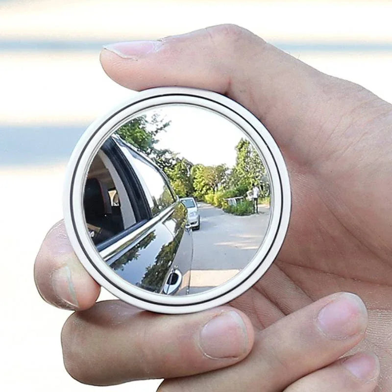 Eine Hand hält einen runden, konvexen Blinden-Rückspiegel, der die Außenansicht reflektiert.