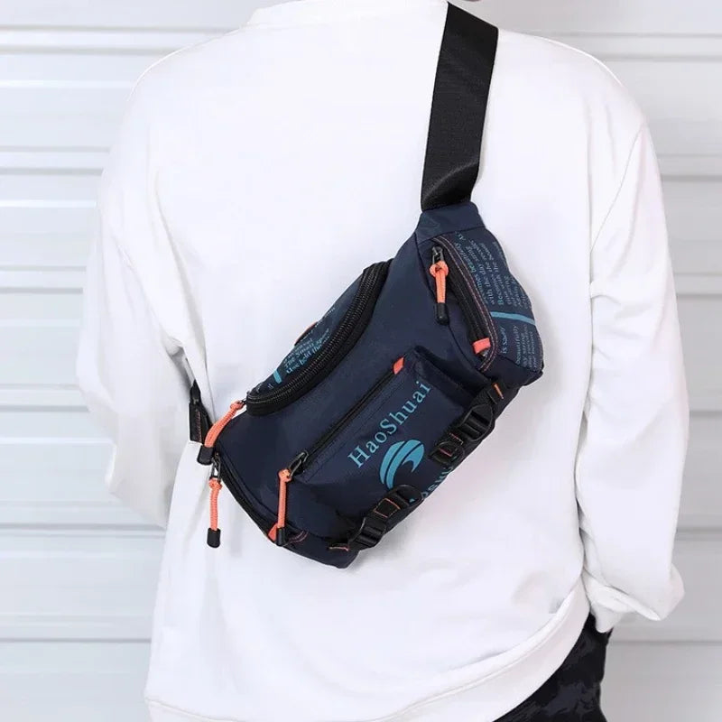 A navy blue tactical chest bag with an orange strap is worn on a white long-sleeved shirt.