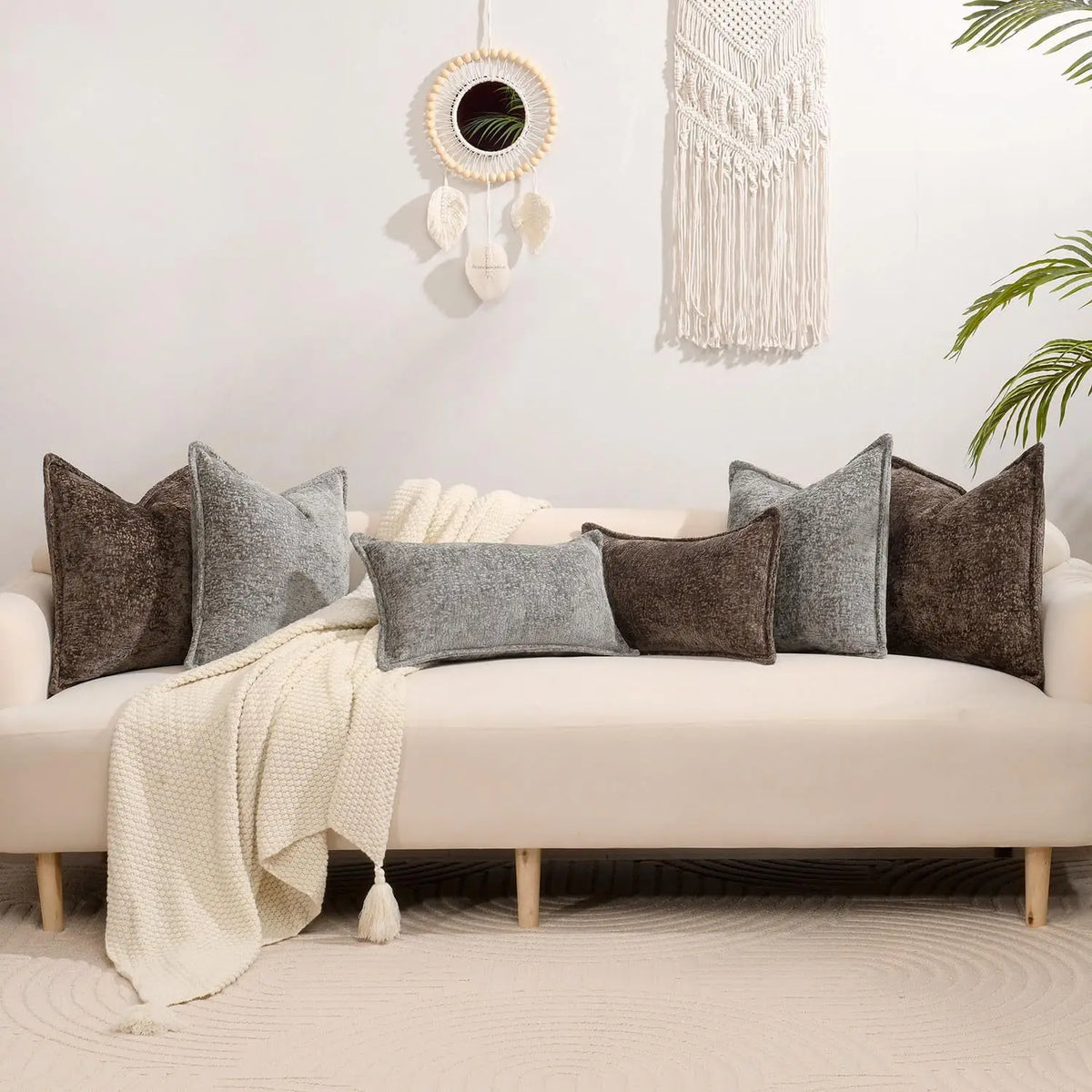 A collection of gray and brown textured square throw pillows arranged on a white sofa with a cream blanket and natural light 