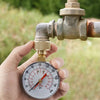 A hand holds a water pressure test gauge with a brass fitting and hose thread, measuring pressure in bars and psi.