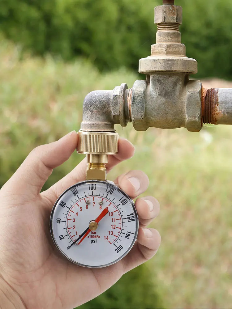 A hand holds a water pressure test gauge with a brass fitting and hose thread, measuring pressure in bars and psi.