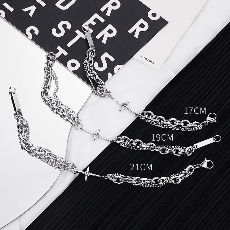 Bracelet en chaîne double couche argenté avec des charms étoile et croix sur fond noir.
