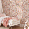 A white wooden bed decorated with pink and peach floral wallpaper and a soft pink blanket.