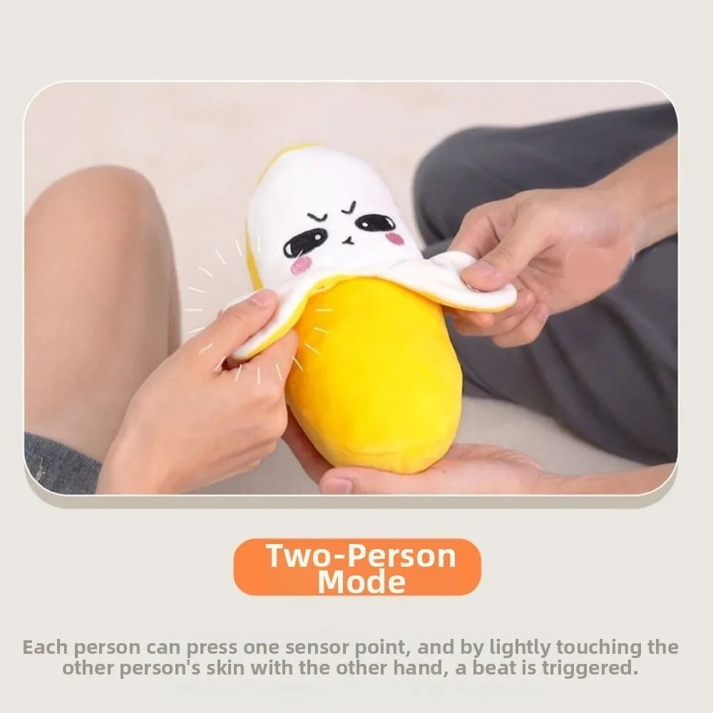 A yellow plush banana toy is being pressed by a hand, demonstrating its two-person touch sensor feature.