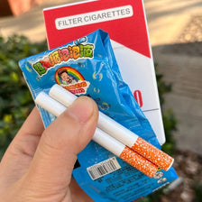 A hand holds a blue packet of funny bubble blowing pipes and a red card labeled Filter Cigarettes.