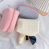 A collection of pink and light gray quilted portable makeup bags with zippers and a white quilted pouch featuring a blue acce