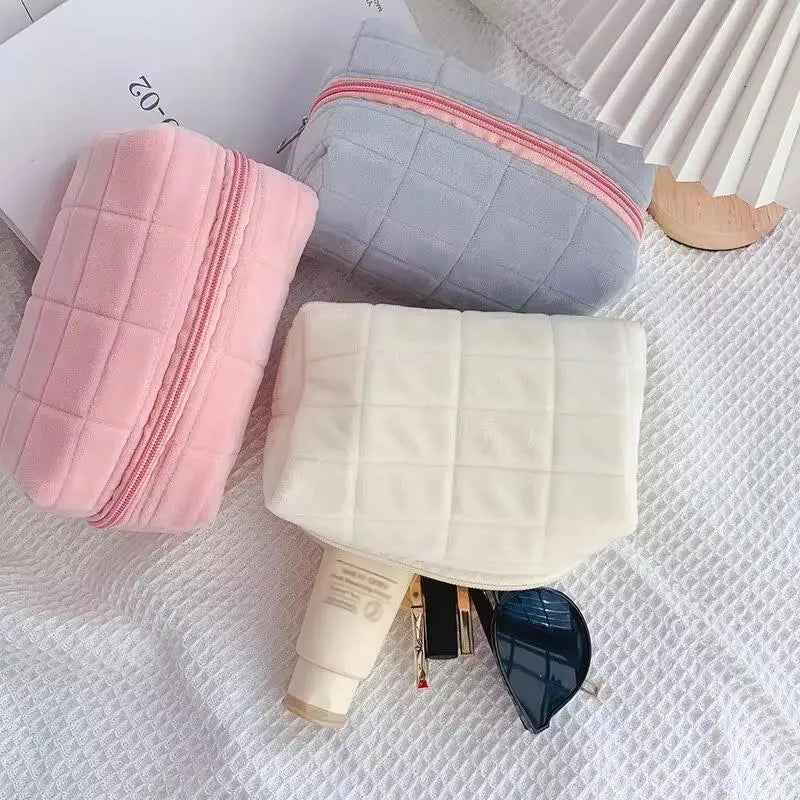 A collection of pink and light gray quilted portable makeup bags with zippers and a white quilted pouch featuring a blue acce