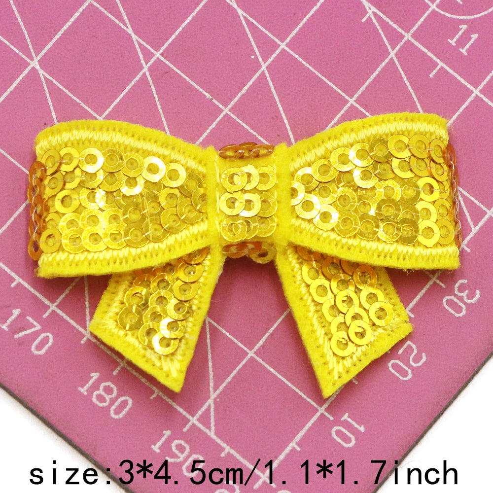 Yellow sequin bow patches for DIY crafts shown on a pink grid background