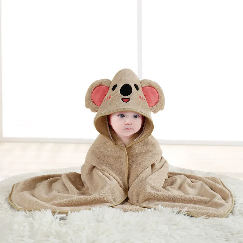 A baby wearing a tan hooded towel with an elephant face design lying on a white surface.