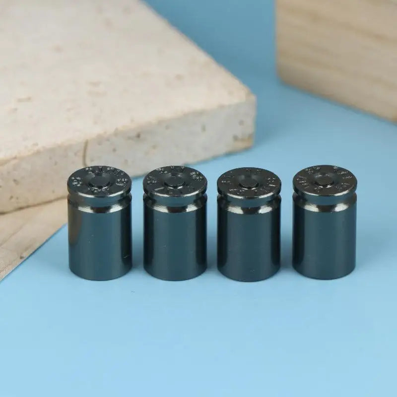 A set of four black bullet shell tire valve stem caps resting on a light blue surface next to a wooden block.
