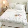 White quilted bedspread set with embroidered floral patterns and white pillows on a bed.