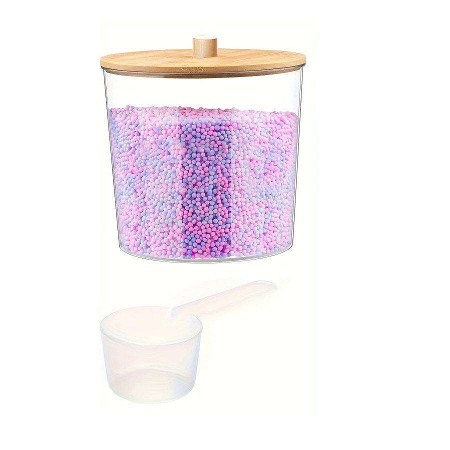 Clear acrylic detergent pod storage container with a wooden lid and a plastic spoon, filled with pink and purple pods.