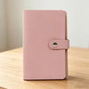 A pink 100-slot cash organizer binder with a snap closure resting on a wooden surface.