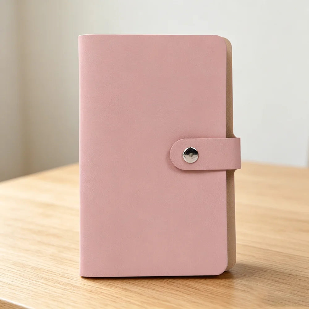 A pink 100-slot cash organizer binder with a snap closure resting on a wooden surface.