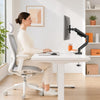 Une femme est assise à un bureau blanc utilisant un bras d'écran réglable robuste pour son ordinateur.