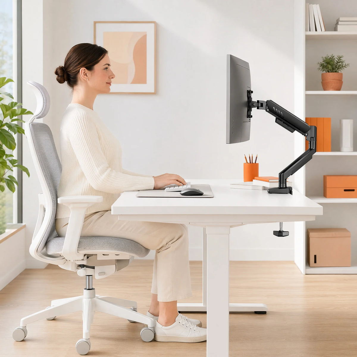 Une femme est assise à un bureau blanc utilisant un bras d'écran réglable robuste pour son ordinateur.