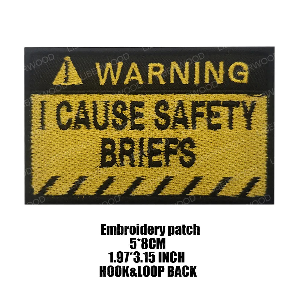 Black embroidered patch with yellow text warning I CAUSE SAFETY BRIEFS