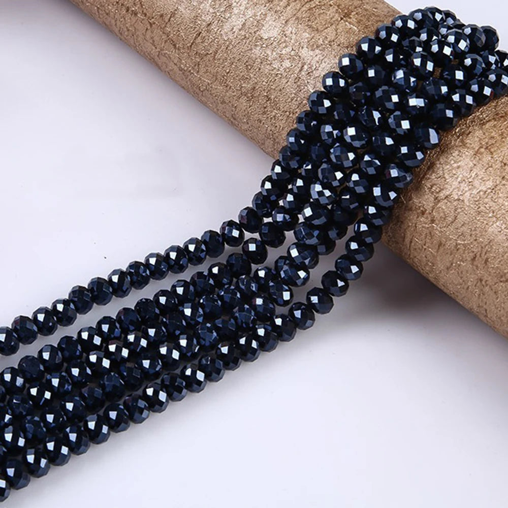 A strand of dark blue faceted crystal glass spacer beads is shown coiled on a natural fiber material.