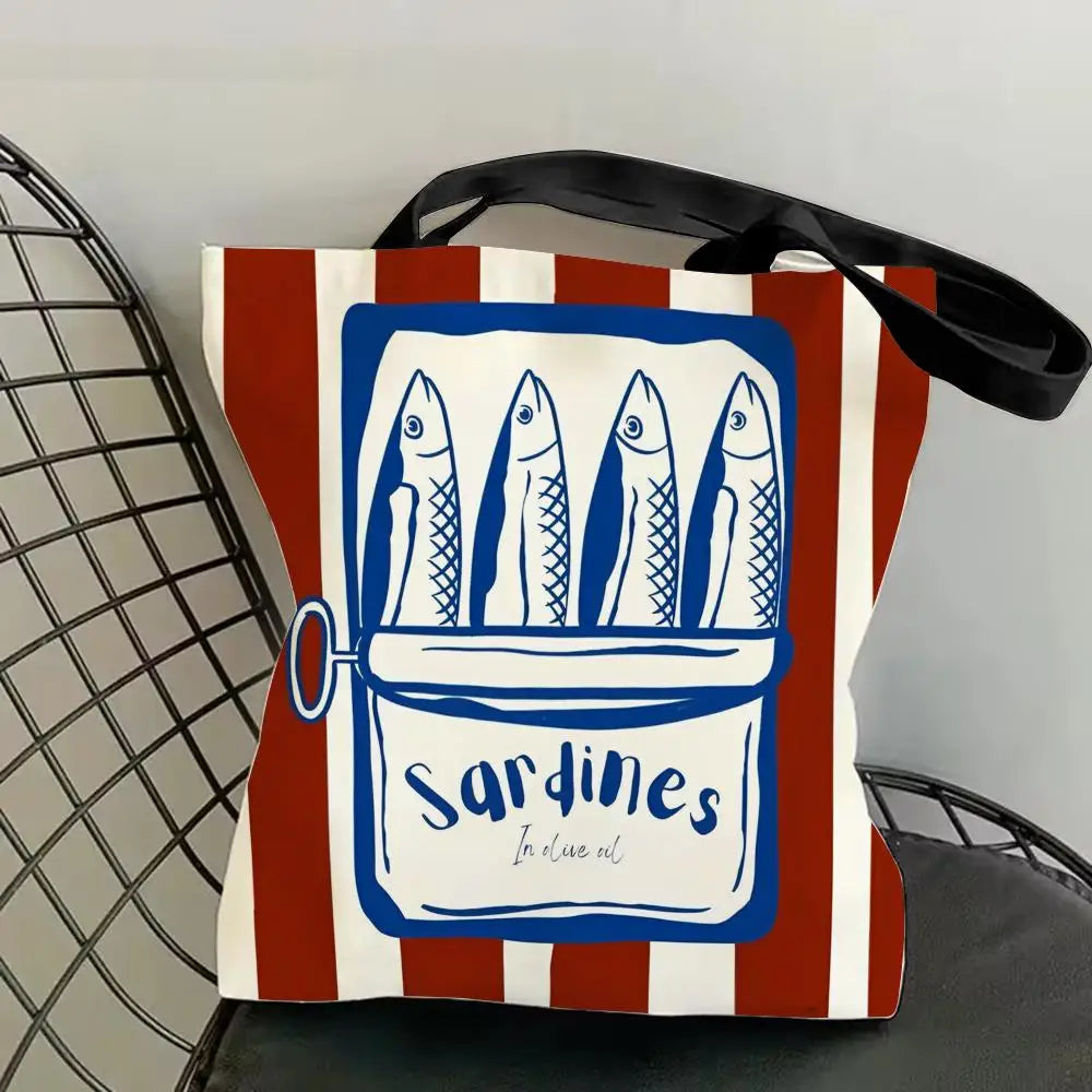A canvas tote bag featuring a blue and white illustration of sardines in a rectangular frame on a striped background.