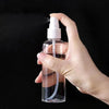 A hand is spraying a clear liquid from a white pump bottle, demonstrating the portable refillable travel spray bottle.