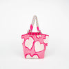 A bright pink tote bag with a white heart pattern and a multicolored braided strap.