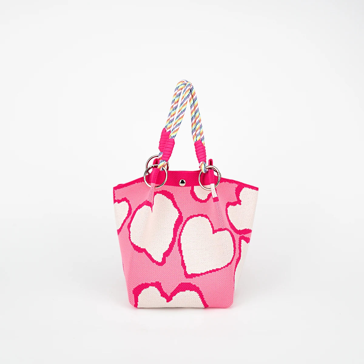 A bright pink tote bag with a white heart pattern and a multicolored braided strap.