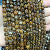 A close-up of natural stone square faceted beads in various shades of brown and gold stacked on a hand.