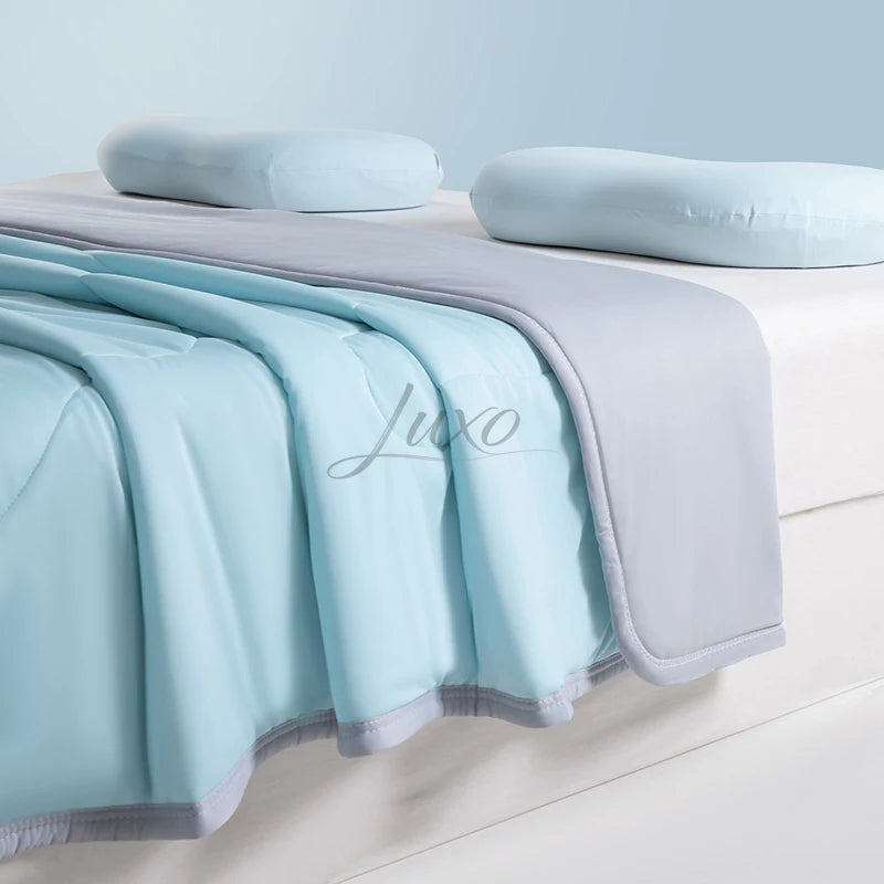 Light blue and gray ice silk cooling blanket draped over a white surface with soft pillows.