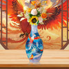 A blue glass vase with a floral arrangement sits on a wooden surface against a background of a red and orange feathered wing 