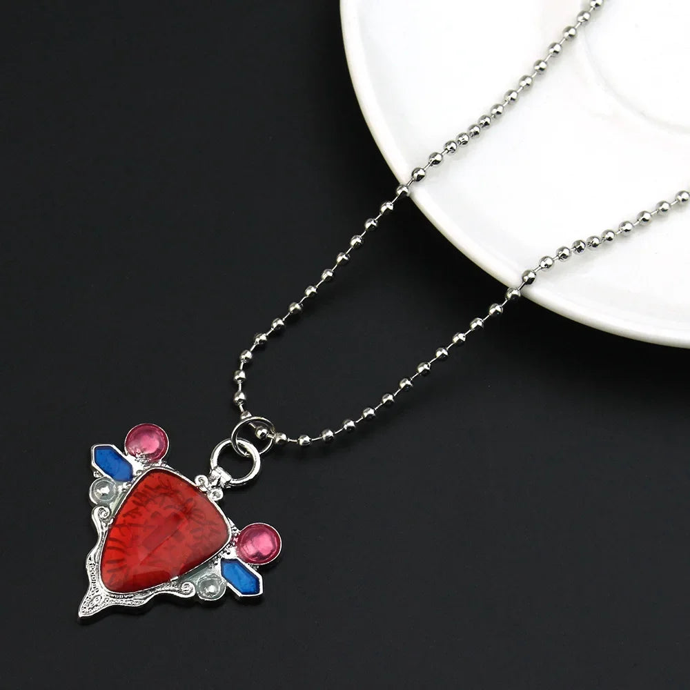 A silver pendant necklace featuring a red stone with blue and pink accents, displayed on a white plate.